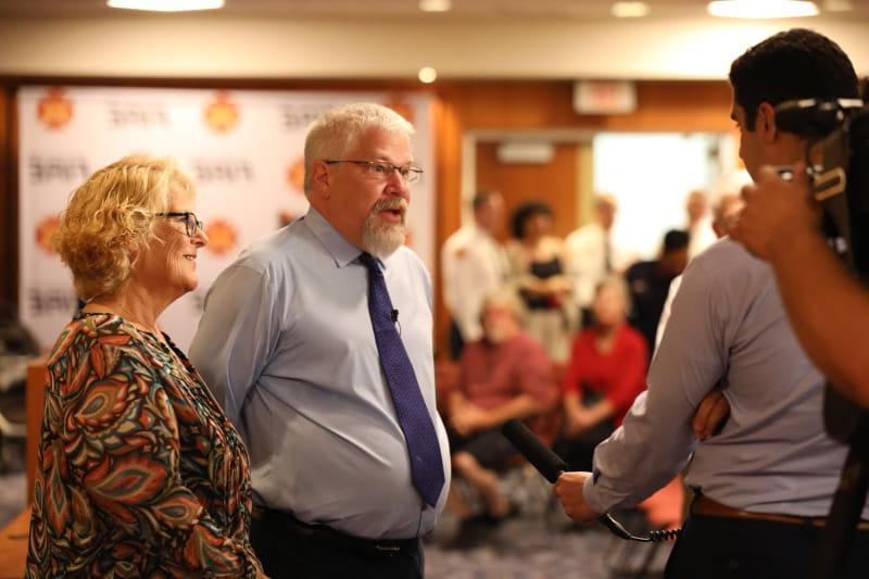 A reporter talks to Mike Button (center) at an appreciation ceremony where Stephanie Button (right) was presented with the 